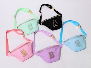 Different colored fanny packs with custom patches sitting together on a table.