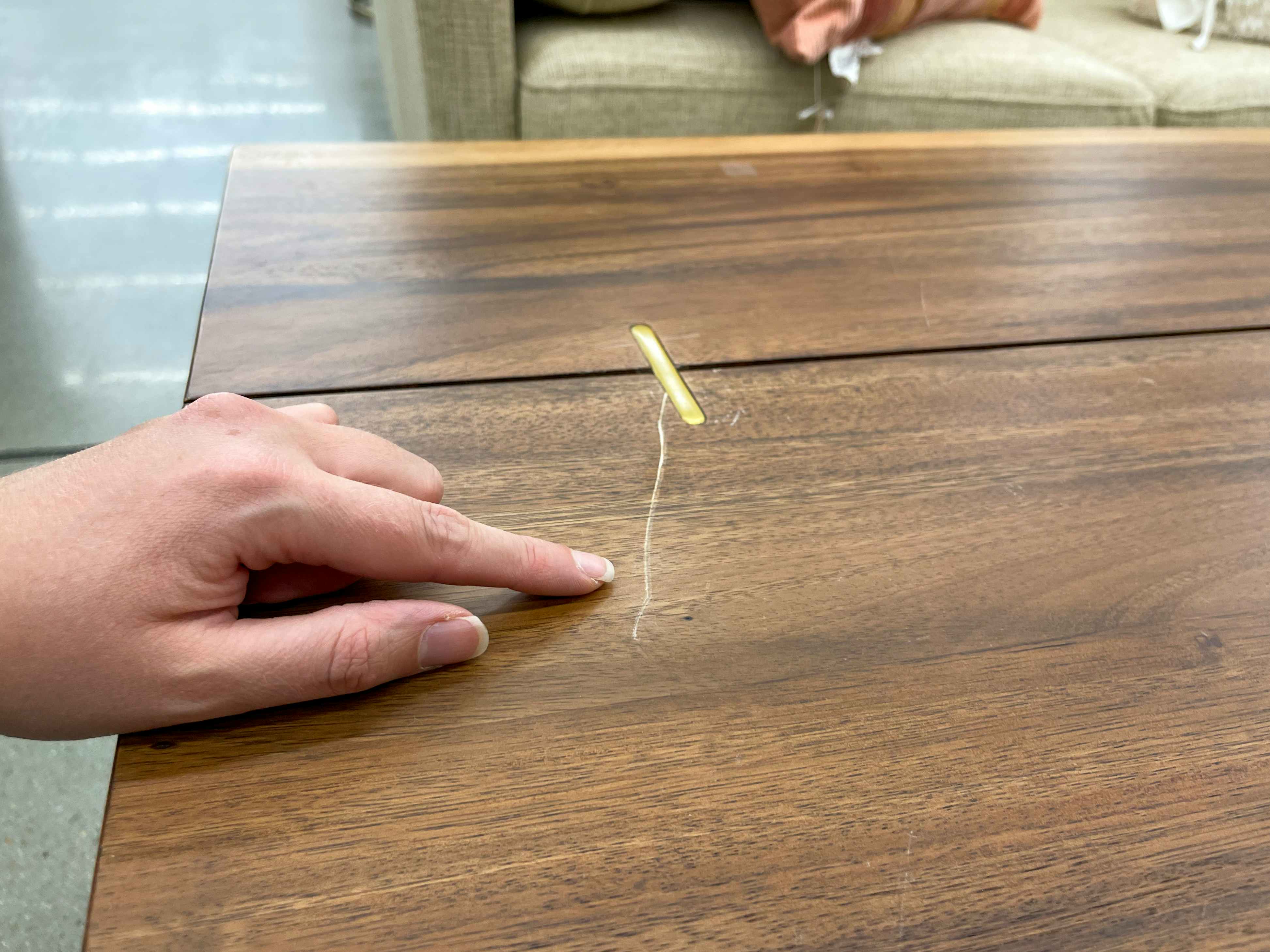 A person pointing out a deep scratch on the top of a coffee table.
