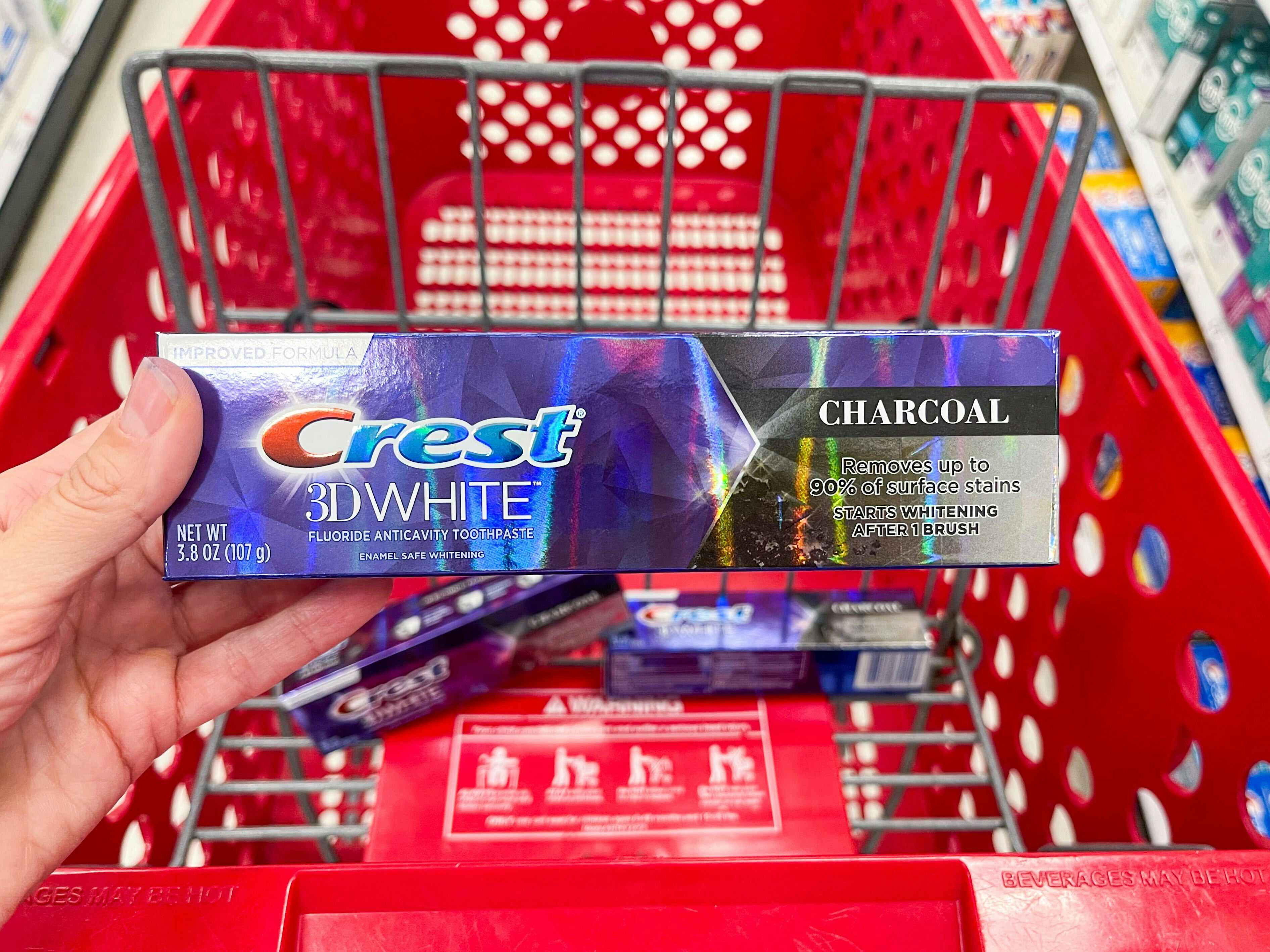 hand holding crest toothpaste box in front of Target shopping cart