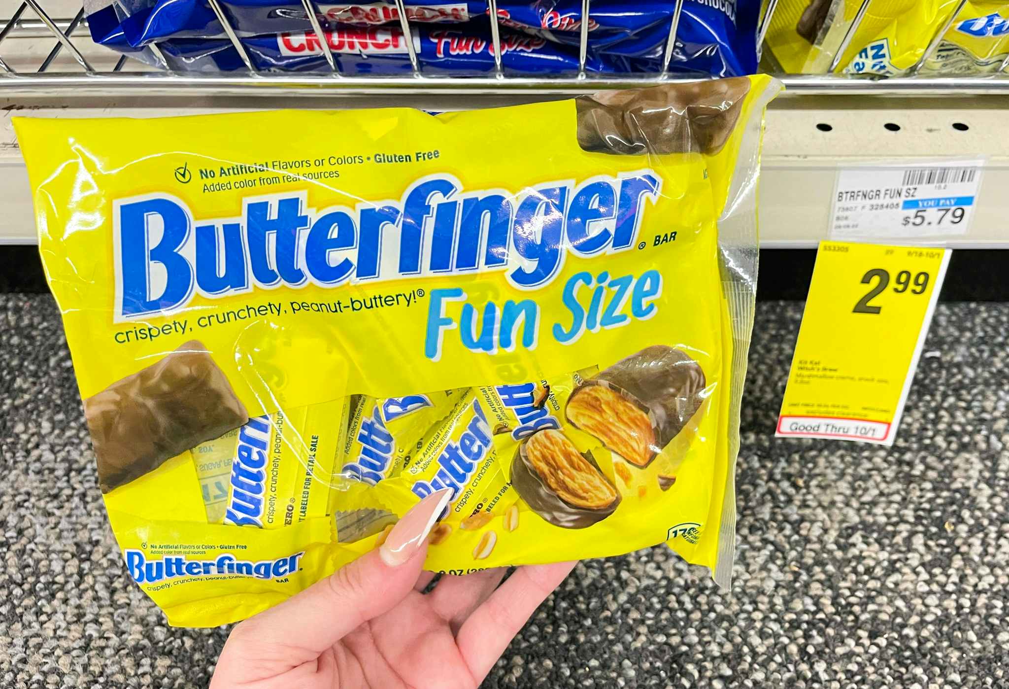 hand holding fun size bag of butterfinger next to sale tag