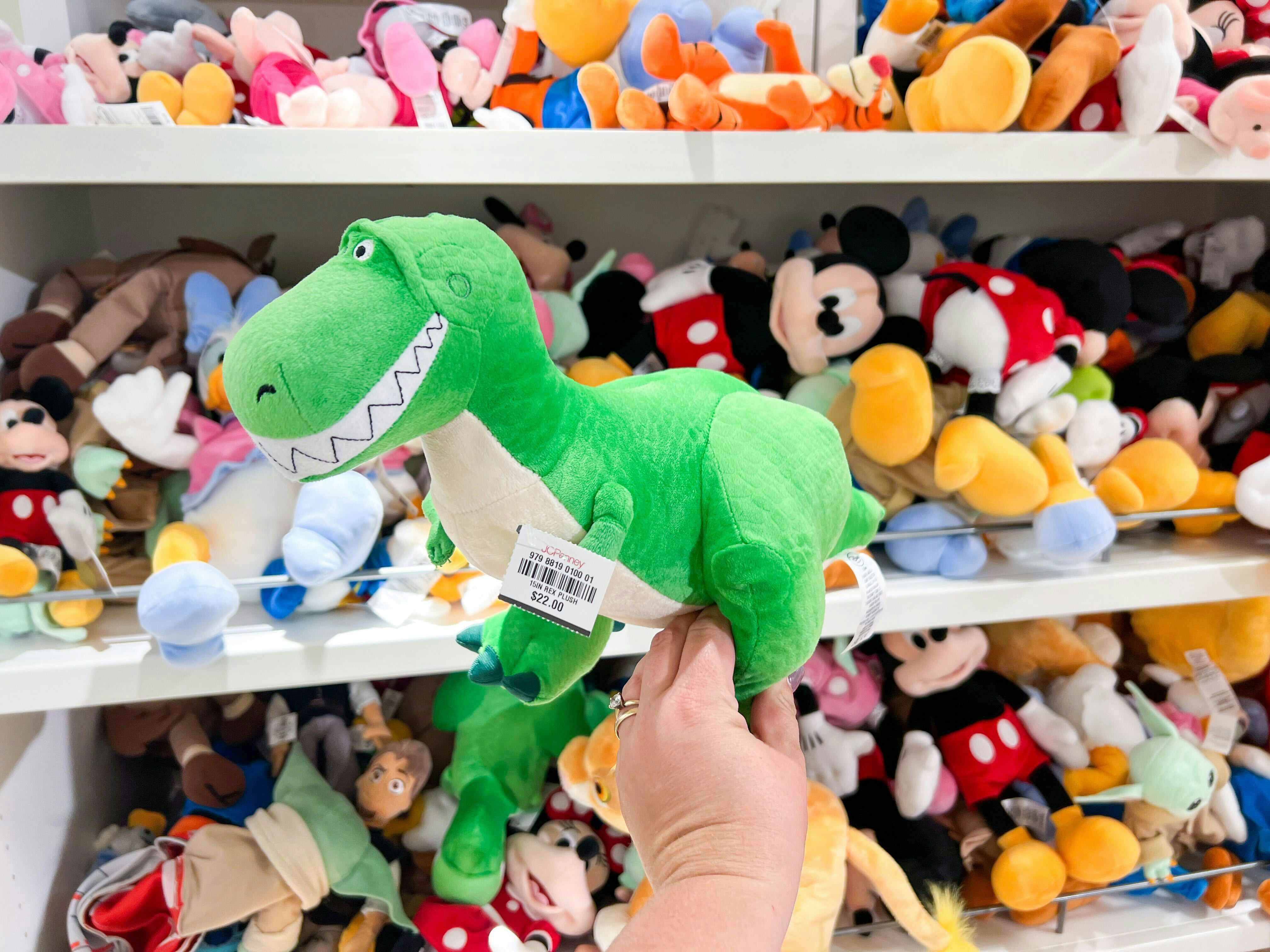 someone holding a rex from toy story plushie in a store