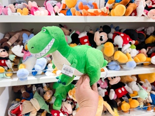 someone holding a rex from toy story plushie in a store