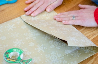 A person folding in wrapping paper to make the bottom of a diy bag.