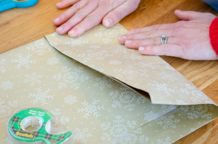 A person folding in wrapping paper to make the bottom of a diy bag.