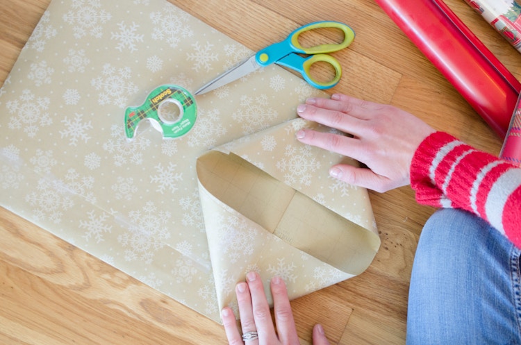 A person folding in wrapping paper to make the bottom of a diy bag.
