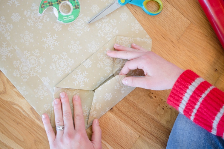 A person using tape to secure the bottom of a DIY wrapping paper bag.