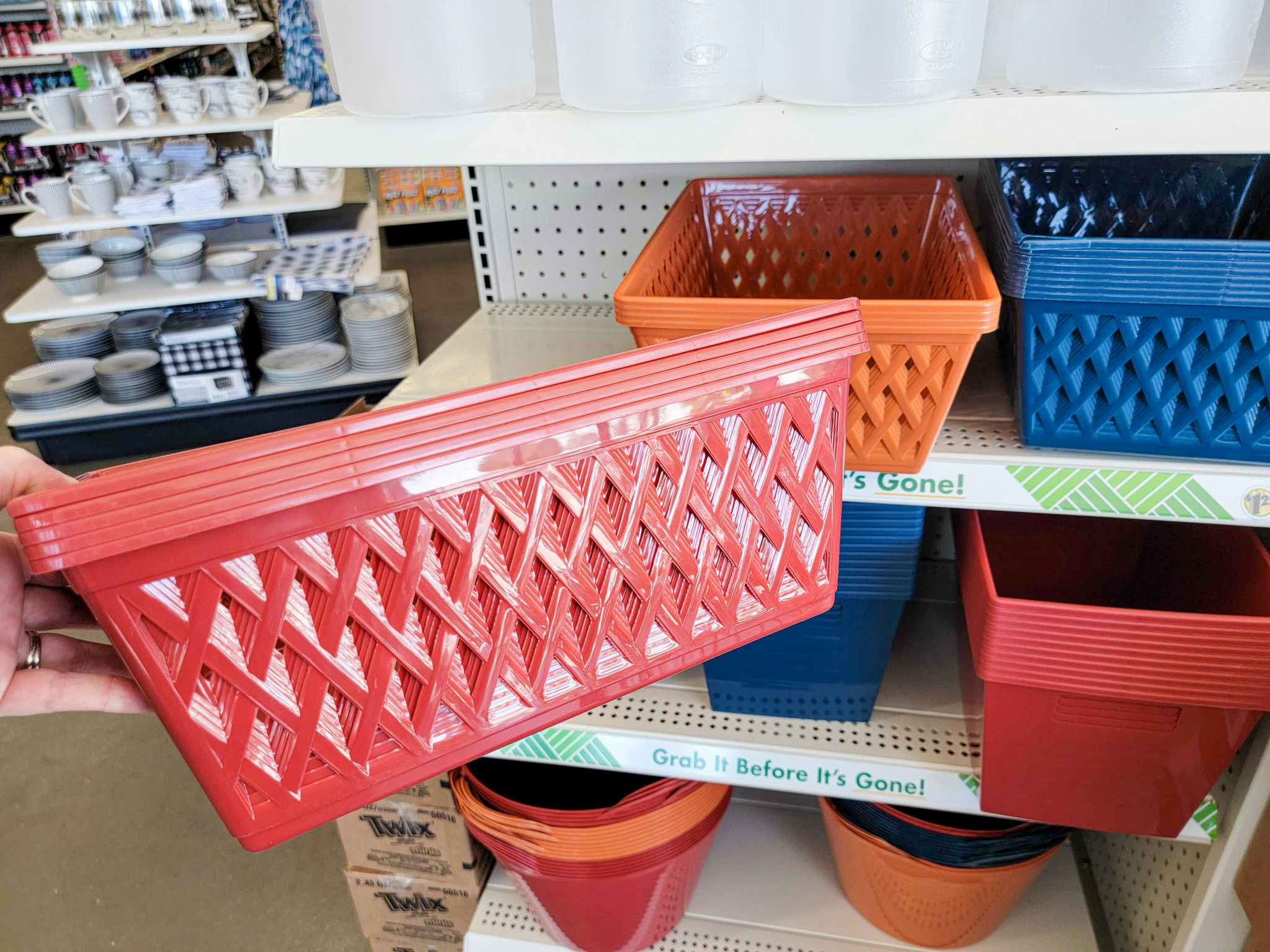 hand holding a dark red storage bin in front of orange and navy bins