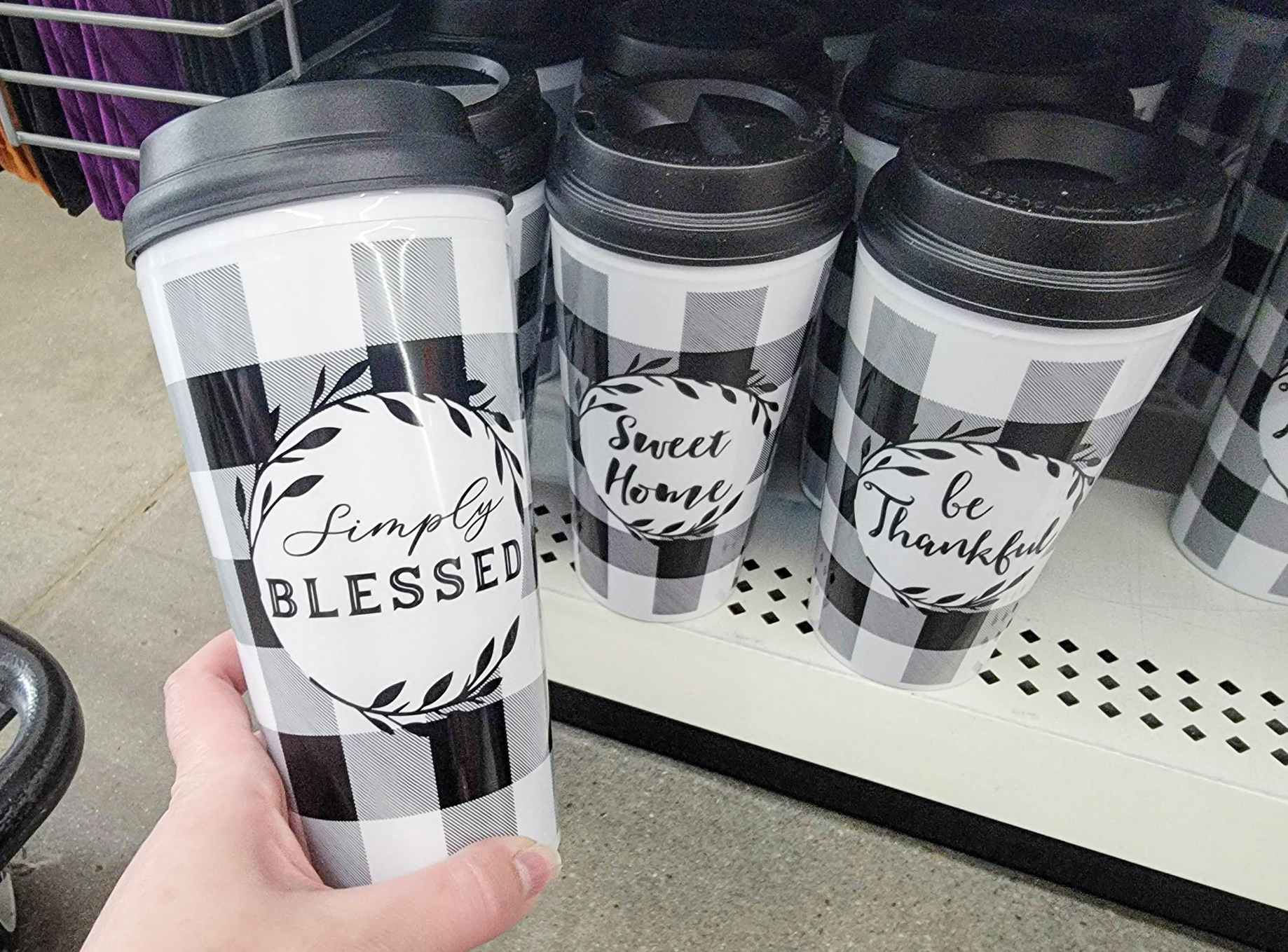 hand holding a to go coffee mug, its white with black buffalo plaid and it says simply blessed, next to other similar mugs