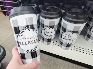 hand holding a to go coffee mug, its white with black buffalo plaid and it says simply blessed, next to other similar mugs