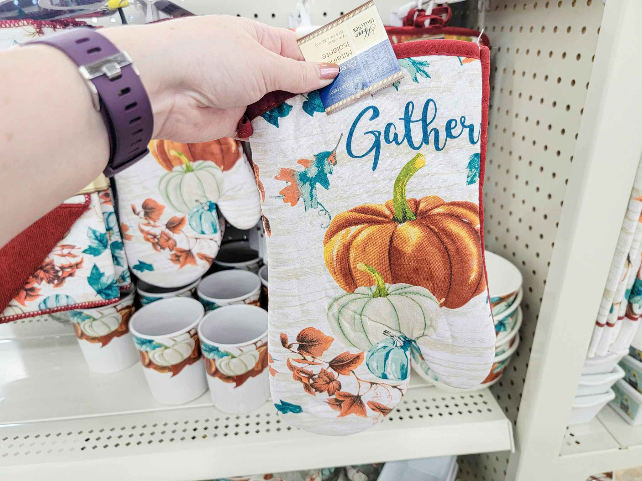 hand holding an oven mitt with pumpkins on it that says gather