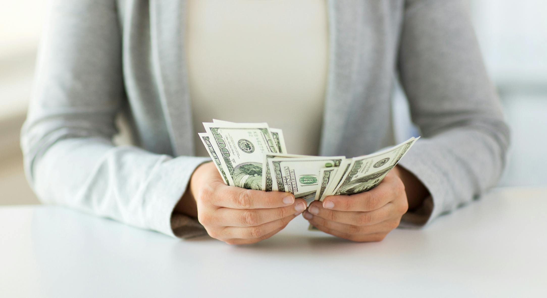 woman sitting at table and holding a lot of cash money