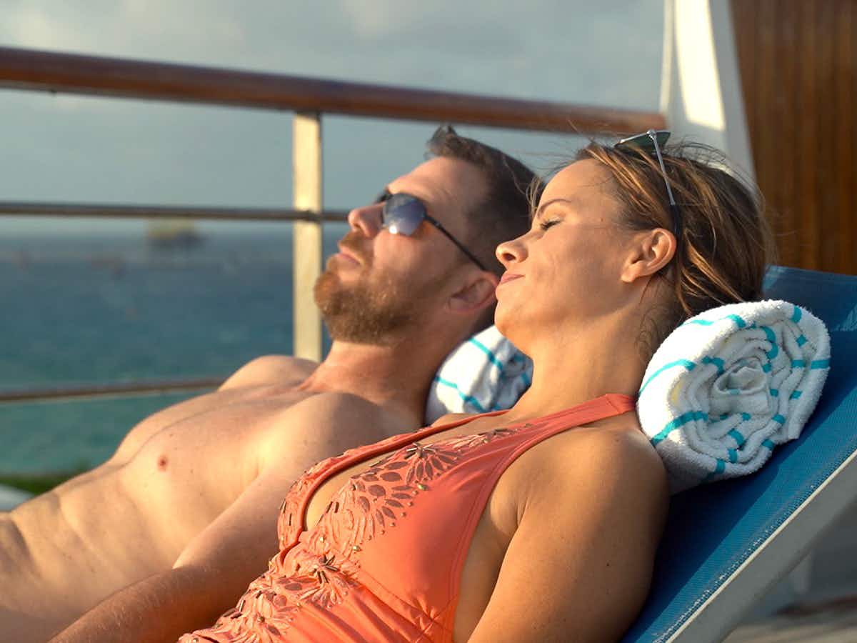 Two people sunbathing together on the deck of the Margaritaville at Sea cruise ship.