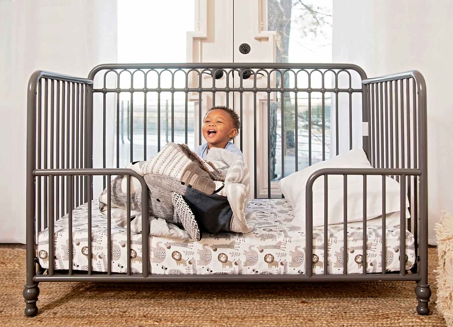 toddler sitting in gray spindle convertible toddler bed