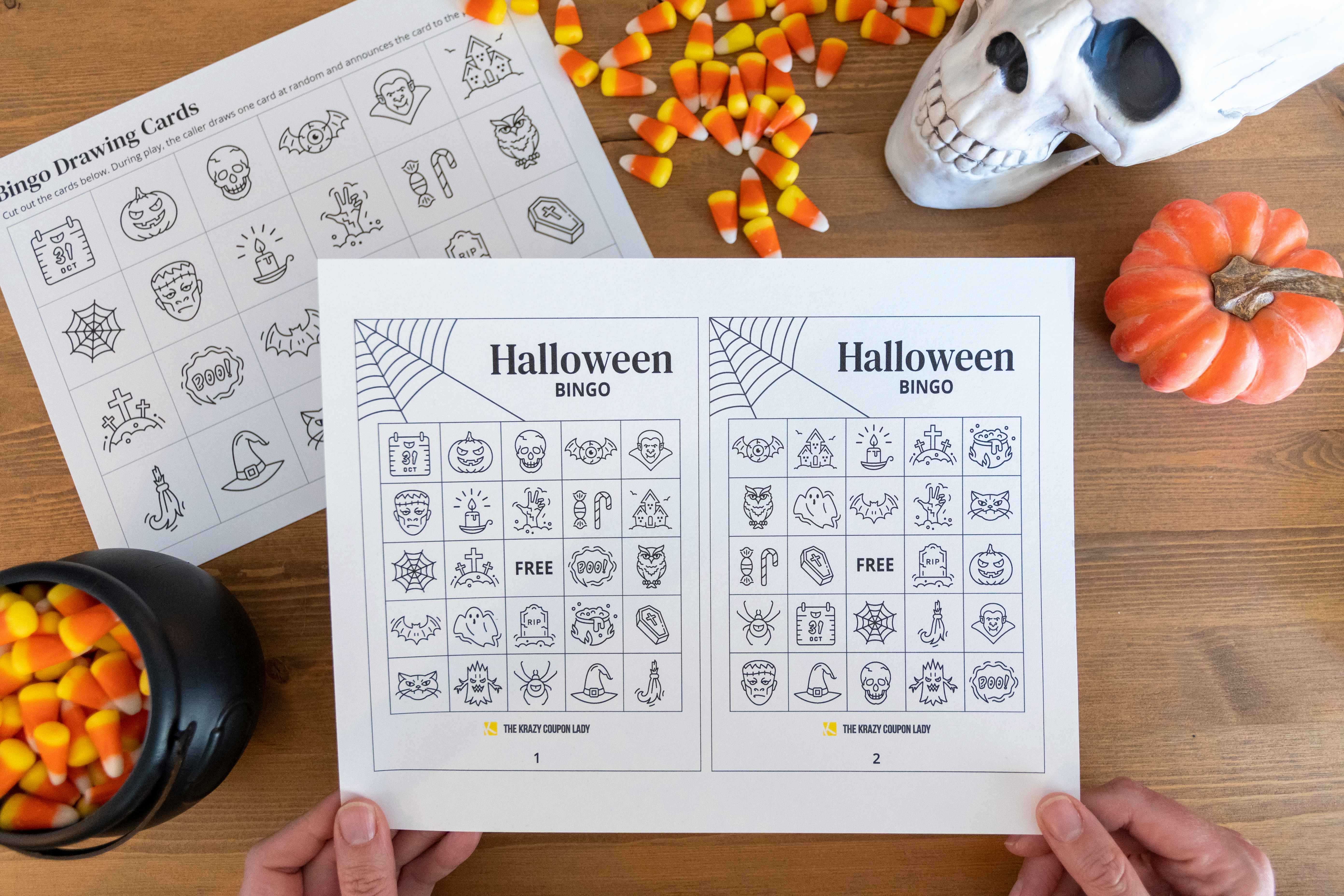 A person holding up a free printable halloween bingo card with candy corn and halloween decor in the background.