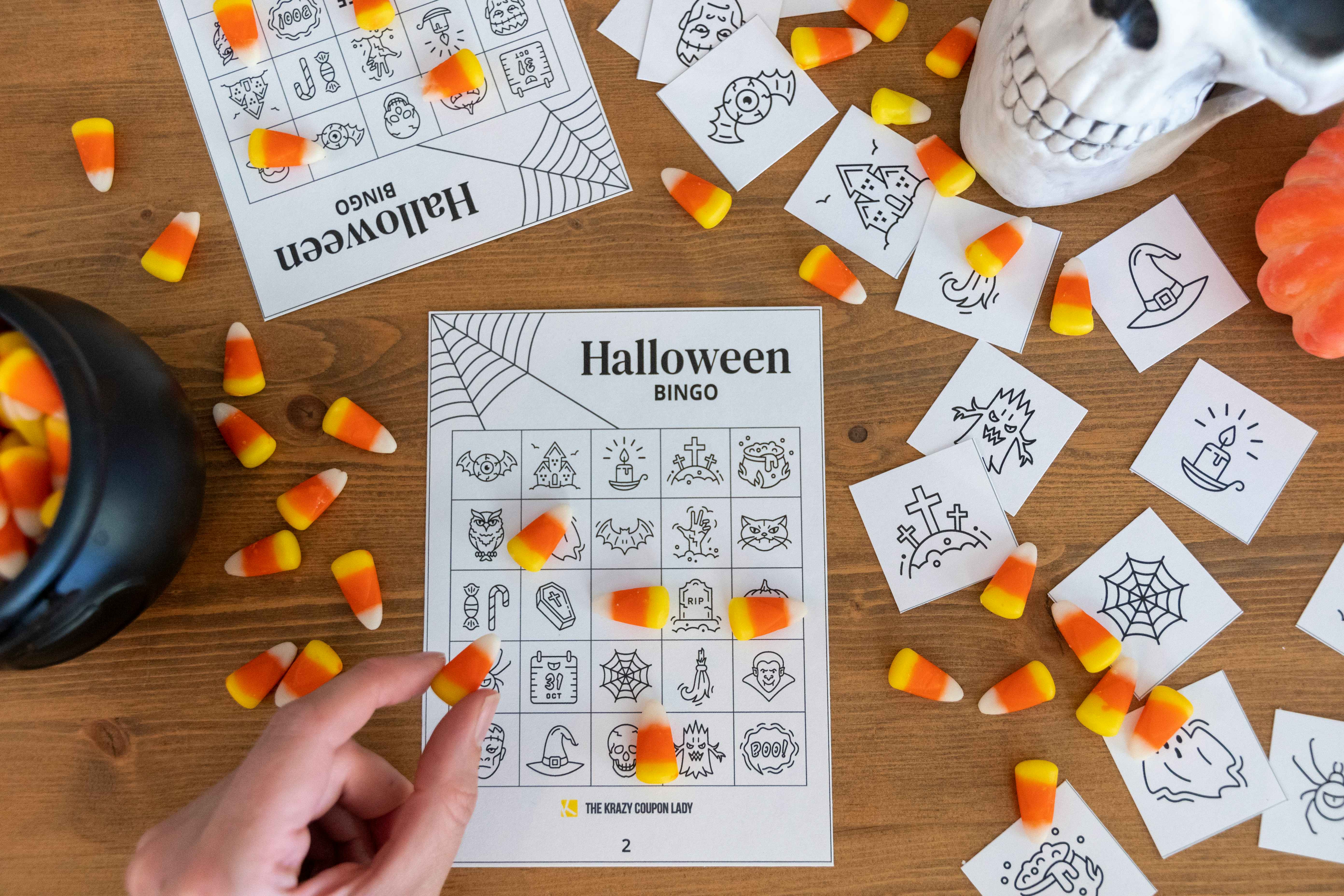 A person placing candy corn on a free printable Halloween bingo card with halloween decor in the background.