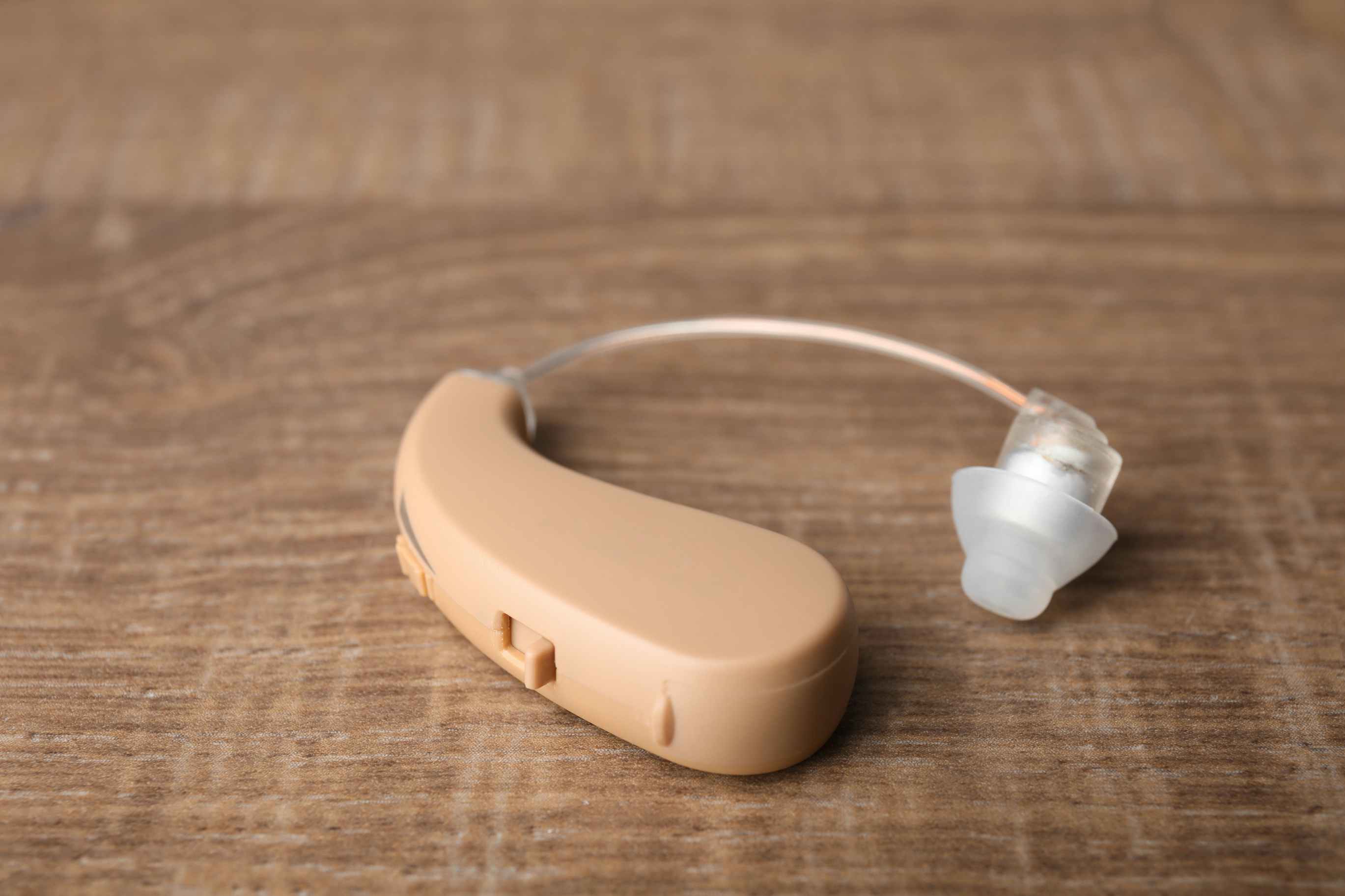 A close up of a hearing aid sitting on a wood table top.