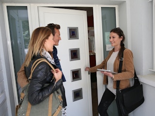 A woman talking to a couple outside of a front door.