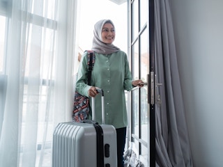 A woman walking into a front door with a suitcase.