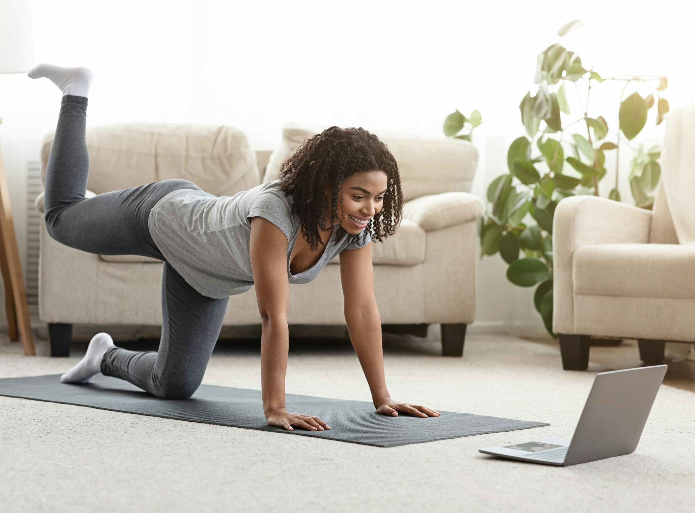 A woman exercising at home while watching a video on a laptop