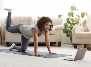 A woman exercising at home while watching a video on a laptop