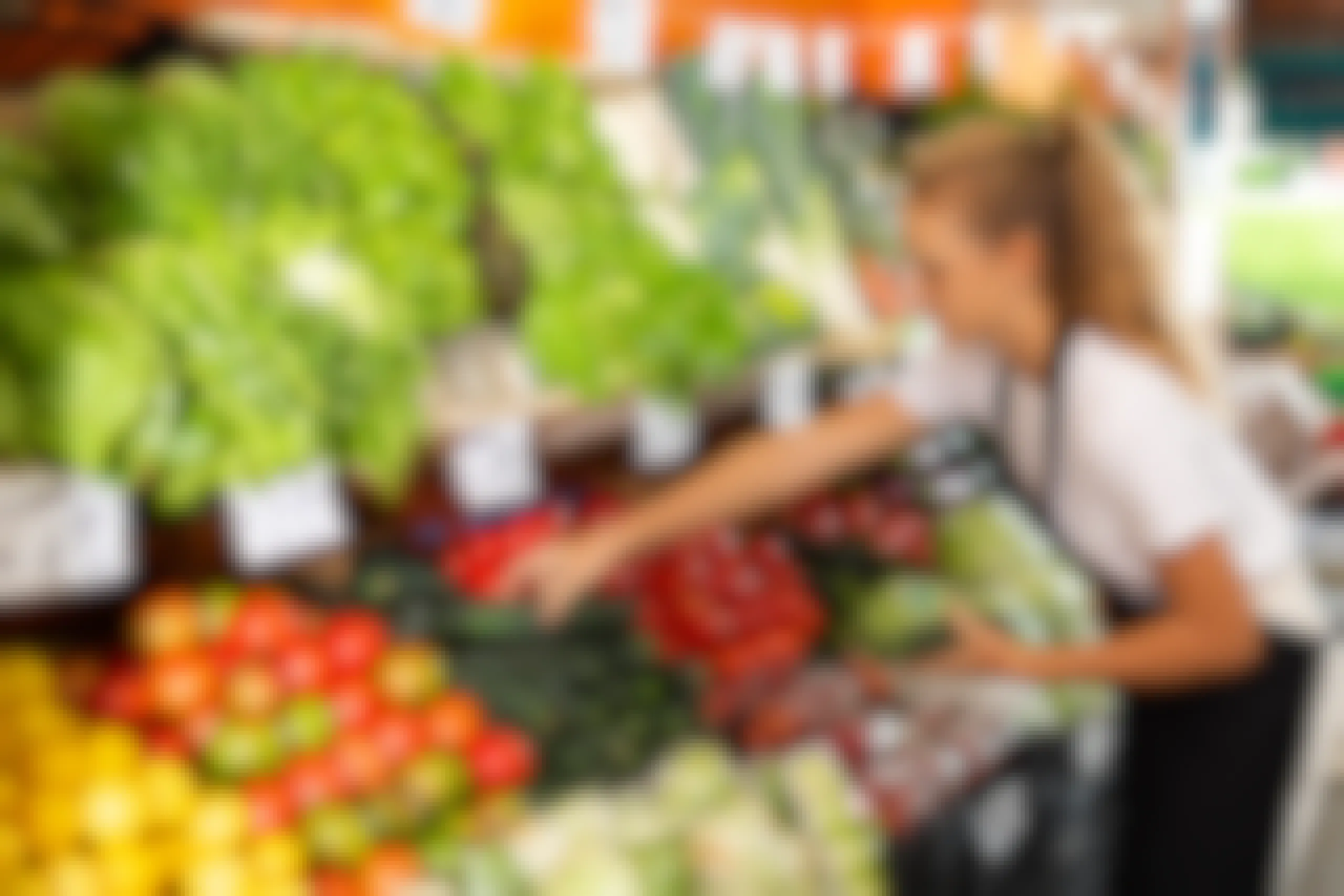teenage girl stocking vegetables in grocery store produce section