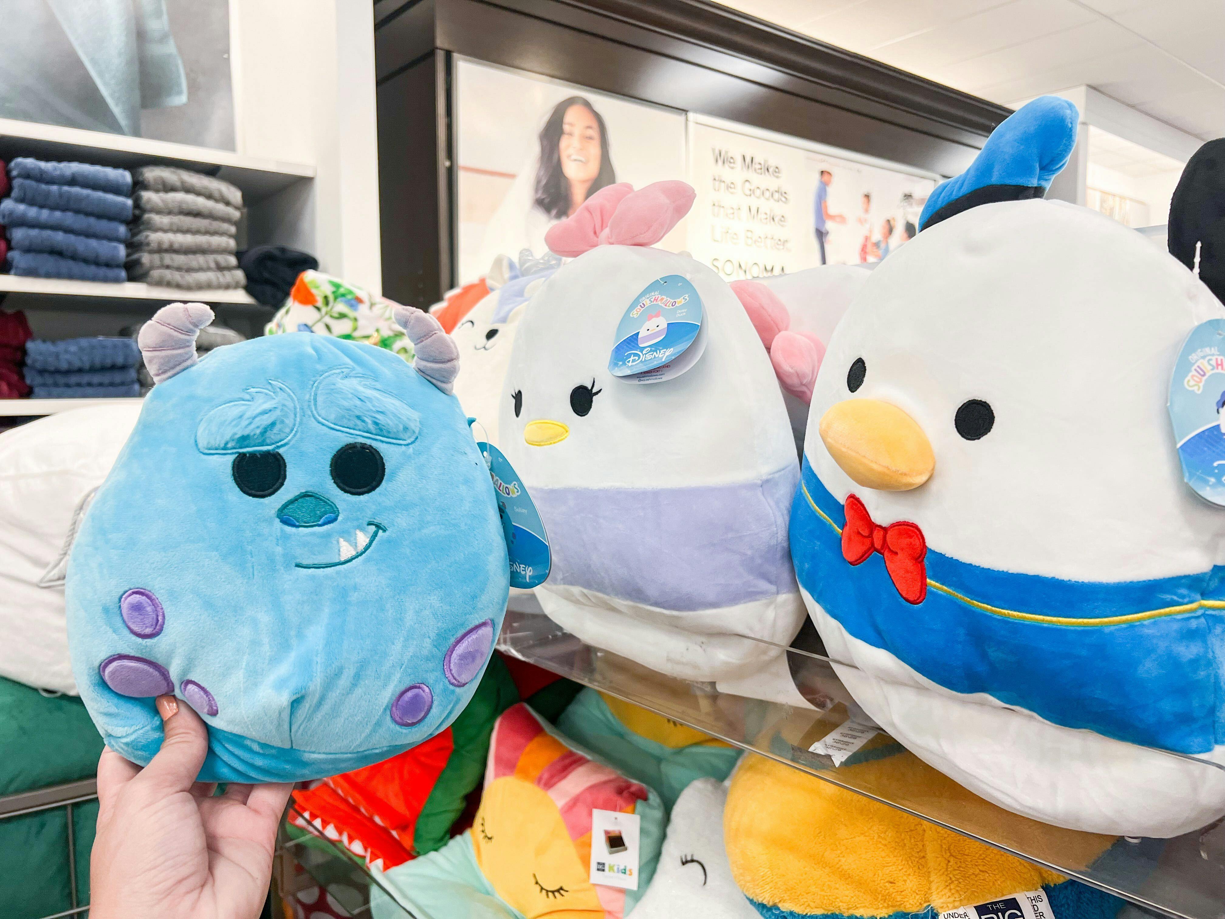 Someone holding a Sully Disney Squishmallow in front of other Disney Squishmallows at Kohl's