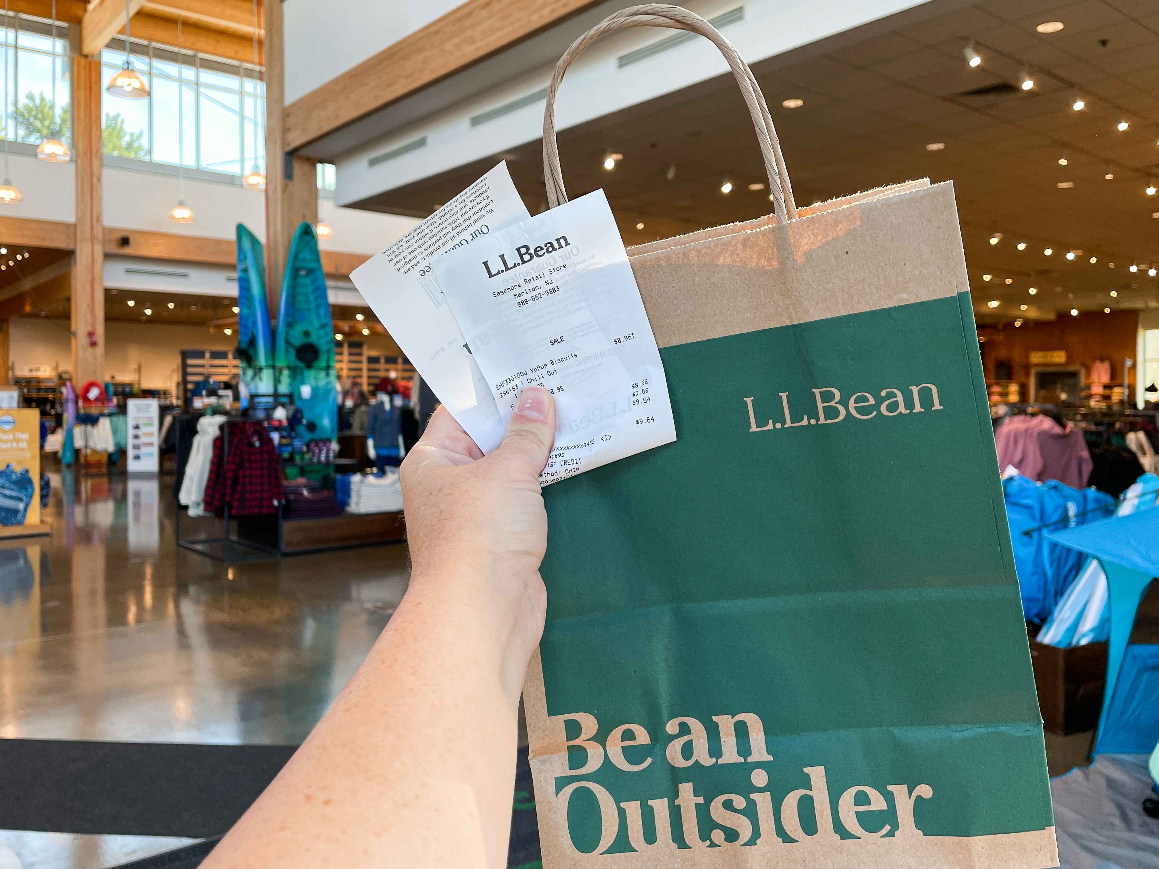 A person's hand holding up a L.L. Bean bag and receipt inside of an L.L.Bean store.