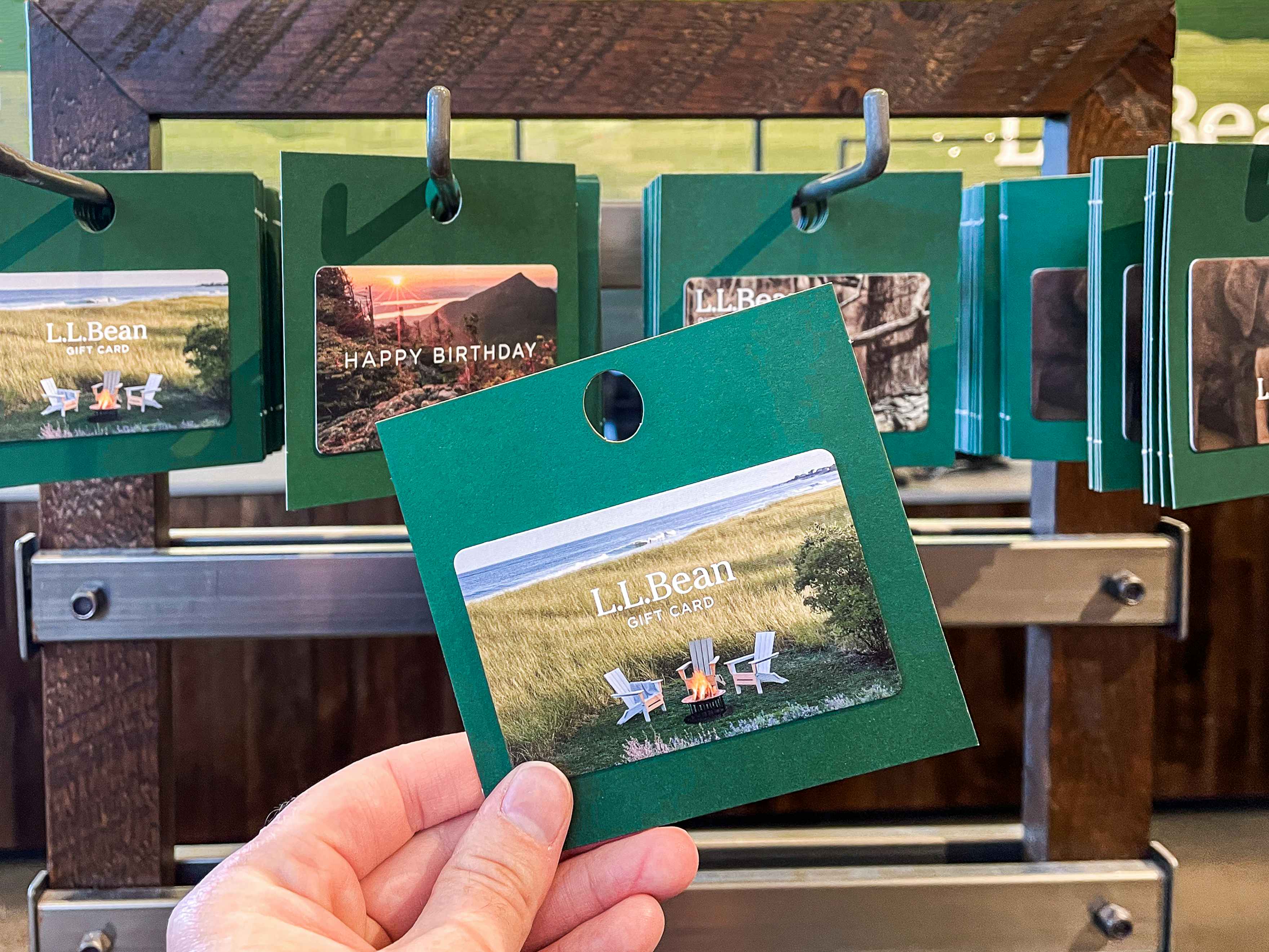 A person's hand holding a L.L.Bean gift card in front of a display of more L.L.Bean gift cards.