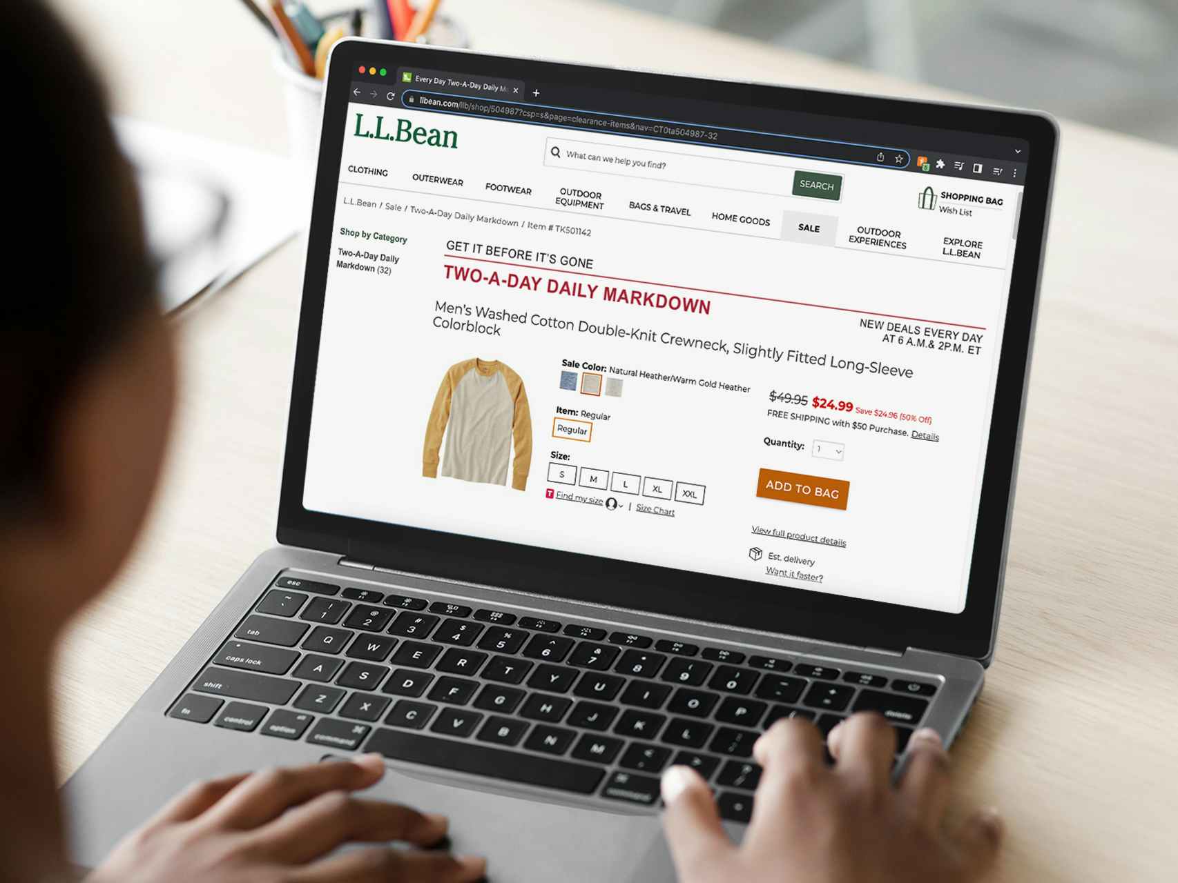A person using a laptop displaying the Two a day daily markdowns on the L.L.Bean website.