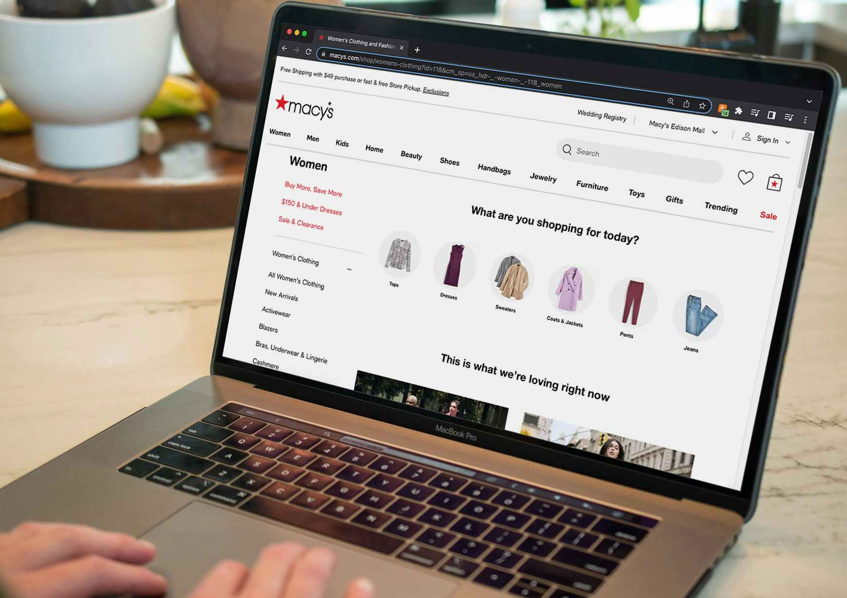 A person using a laptop displaying the women's clothing page on the Macy's website.