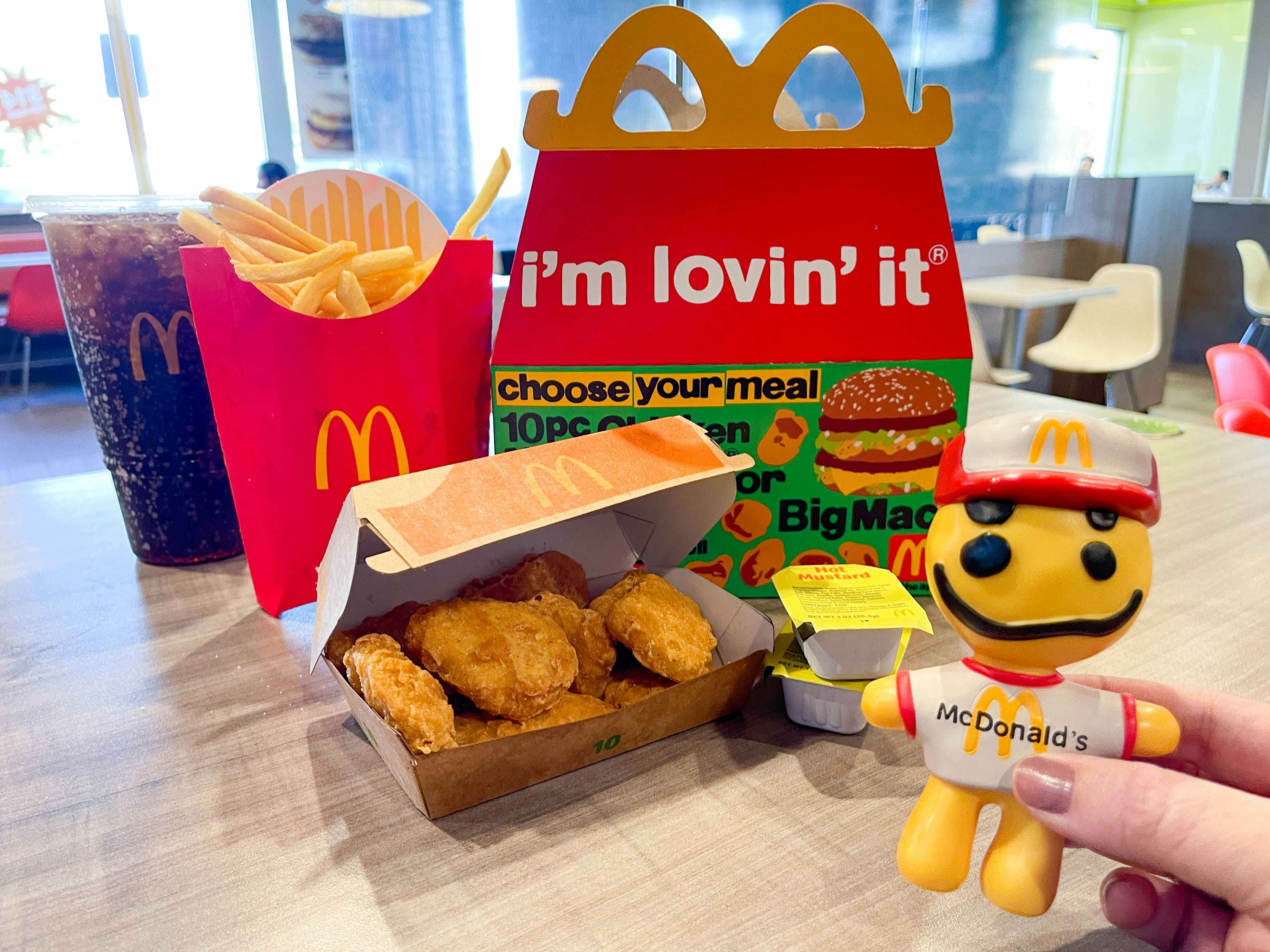 A mcdonalds chicken nugget adult happy meal on table top with toy being held in front