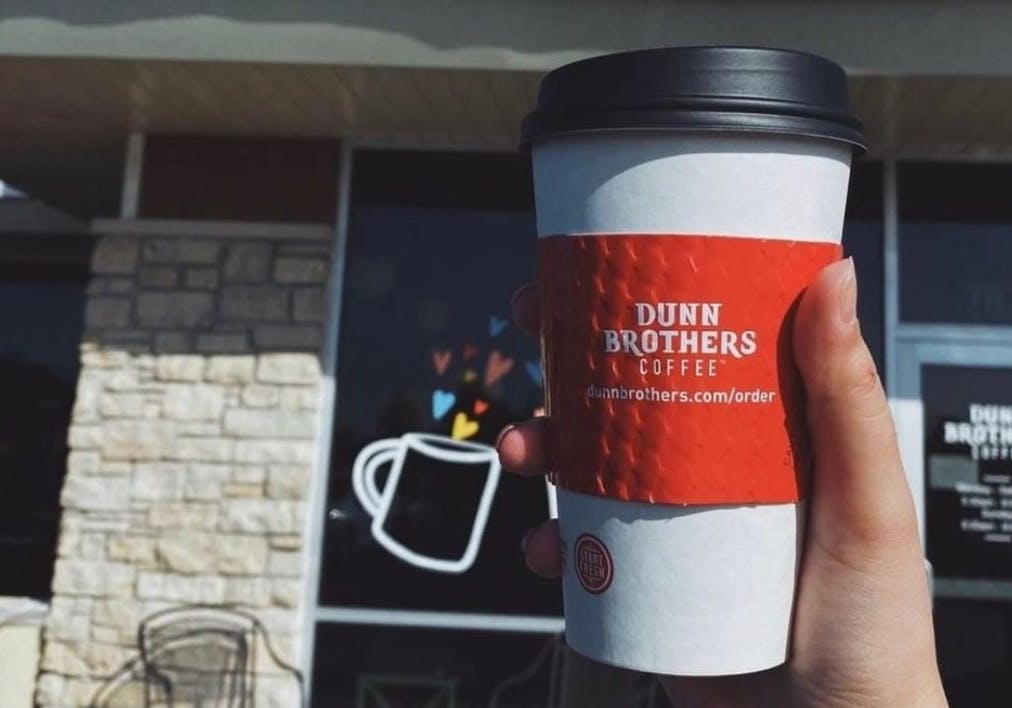 A person holding cup of coffee from dunn brothers