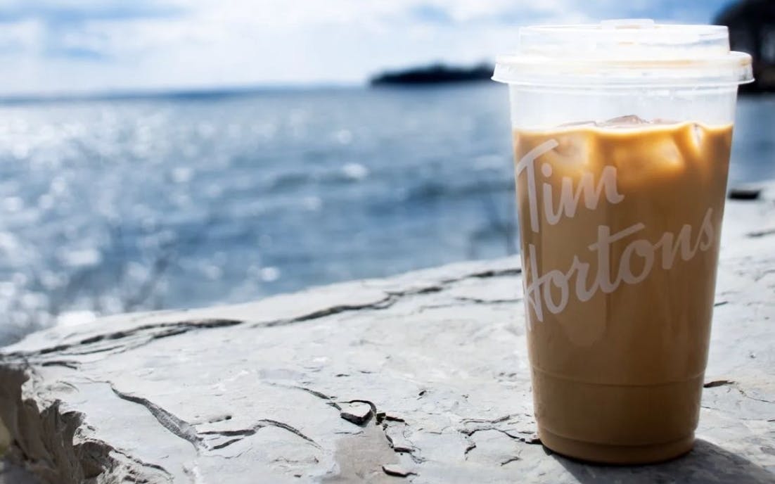 tim hortons iced coffee sitting on a rock with a lake in the background. 