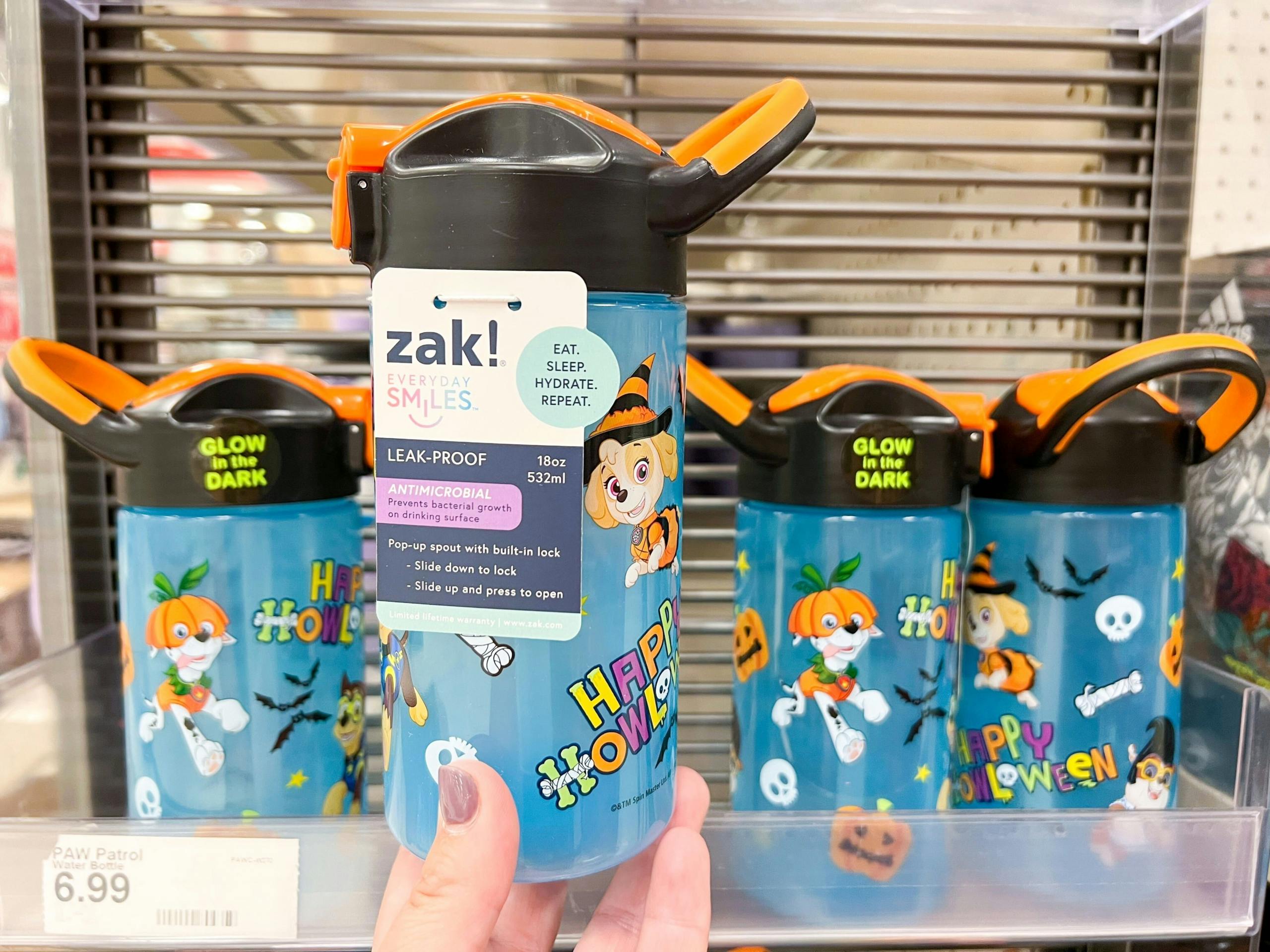 hand holding paw patrol water bottle in front of other water bottles