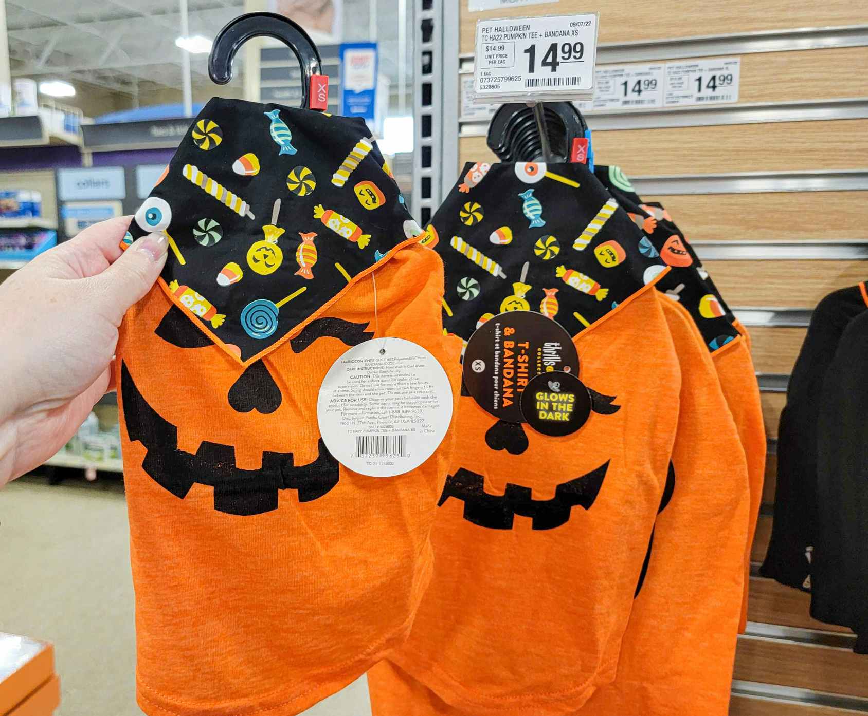 hand holding an orange dog tee with a pumpkin face, and it comes with a candy decorated bandana