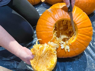 a person pulling the bottom out of a cut pumpkin