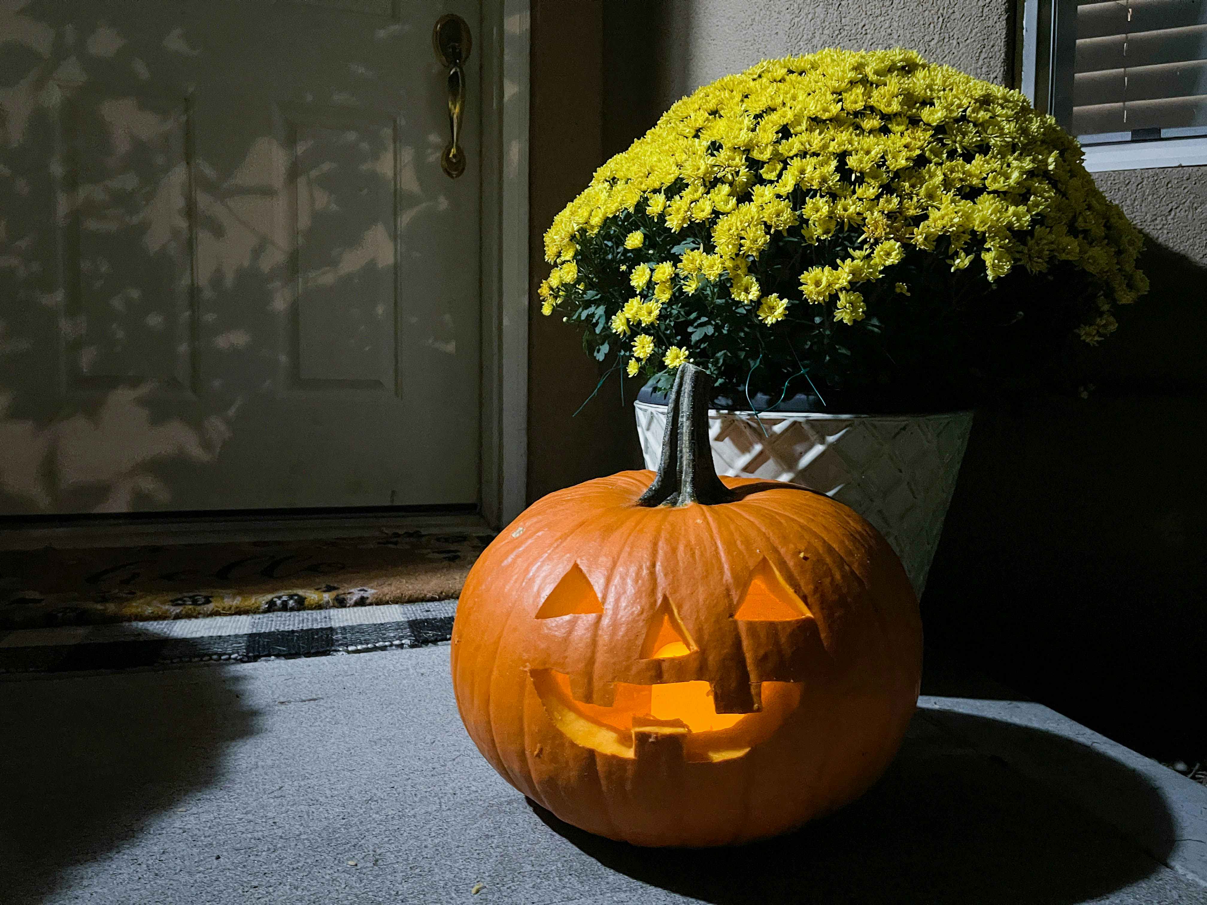 a jack o lantern pumpkin glowing outside in front of a house dorr step