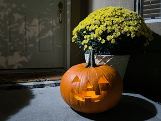 a jack o lantern pumpkin glowing outside in front of a house dorr step