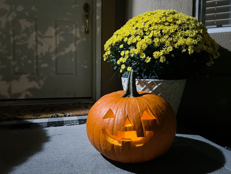 a jack o lantern pumpkin glowing outside in front of a house dorr step