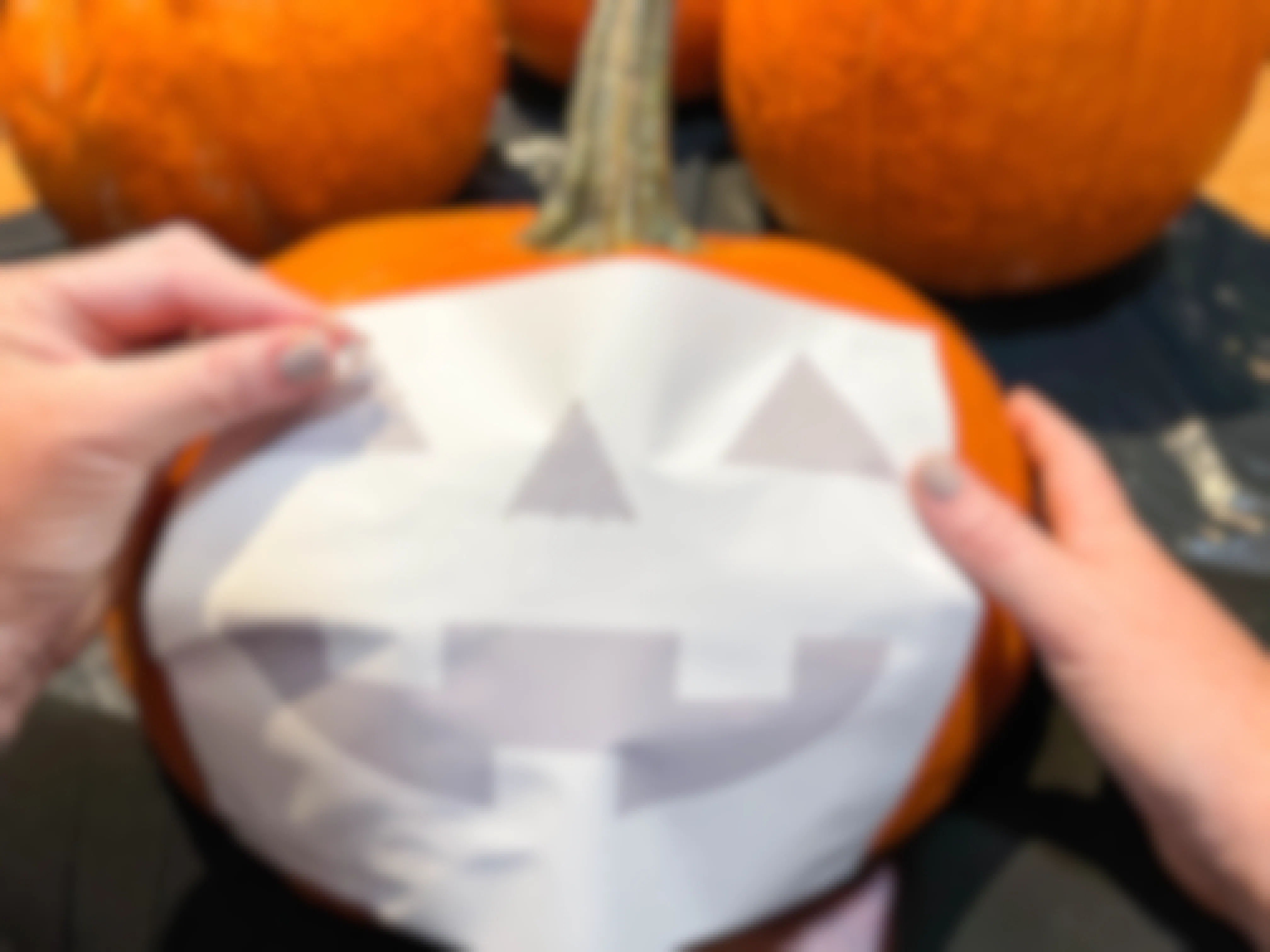 a person tracing a jack o lantern face with push pin on a pumpkin