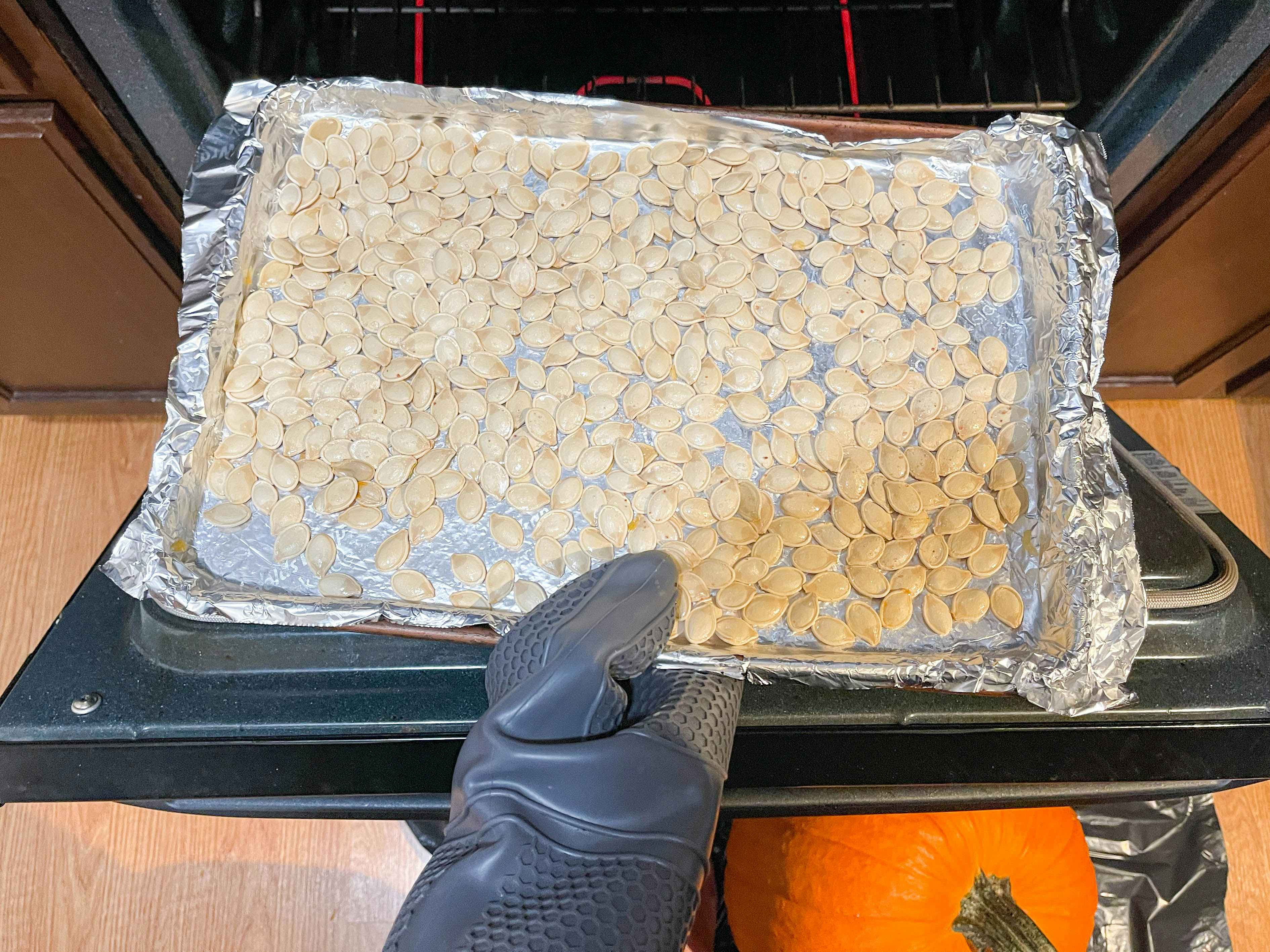 a person putting in the oven a baking sheet with pumpkin seeds 