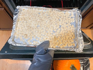 a person putting in the oven a baking sheet with pumpkin seeds