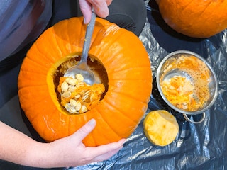 a person using a large spoon to scoop out pumpkin seeds