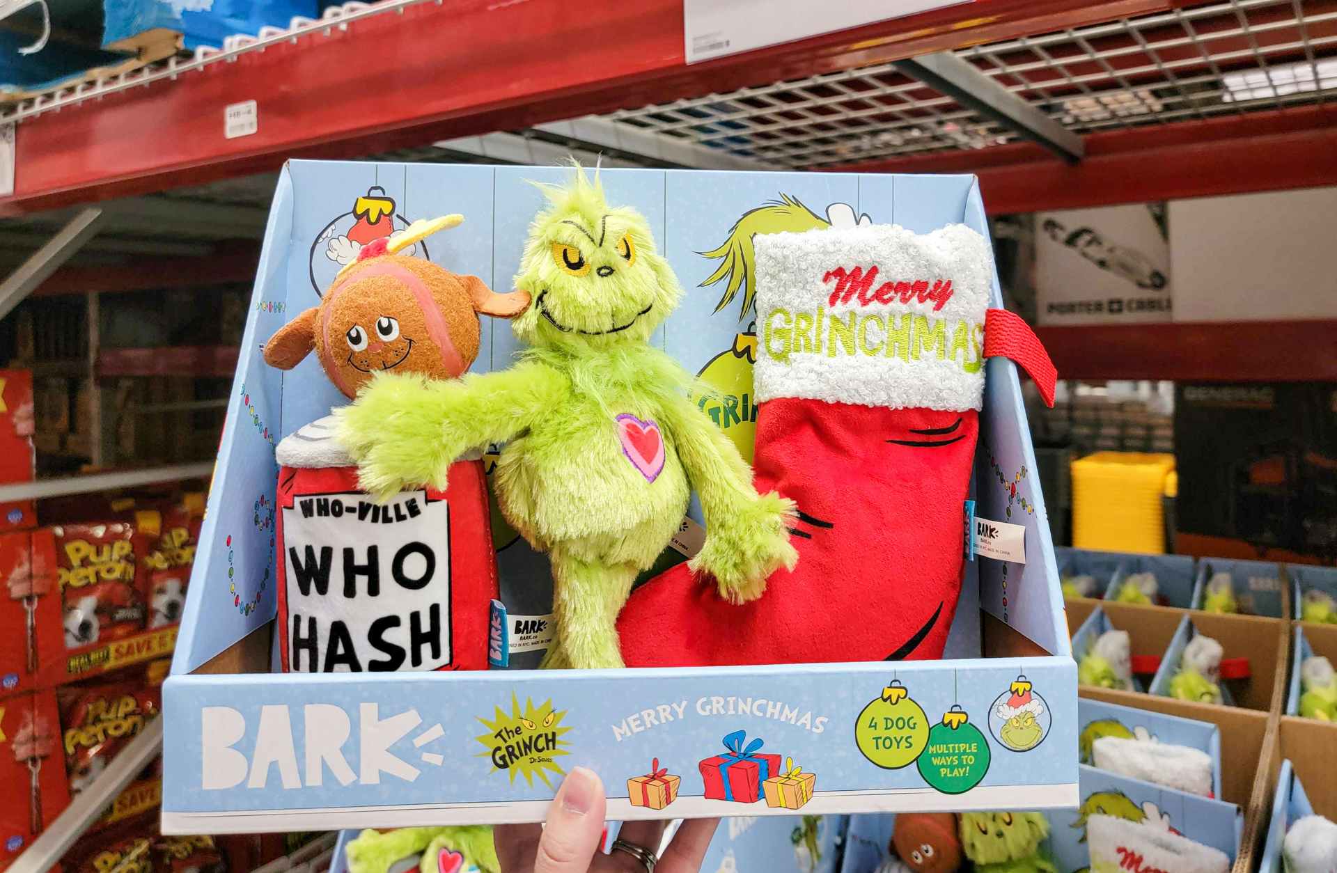 hand holding a 4-pack of grinch dog toys by bark