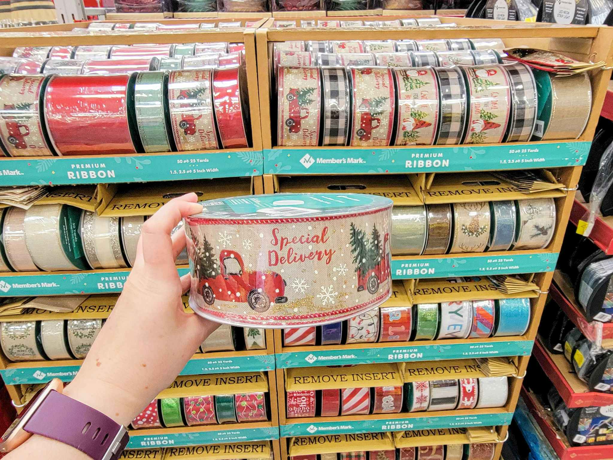 hand holding a roll of christmas ribbon that says special delivery in front of a display of christmas ribbon