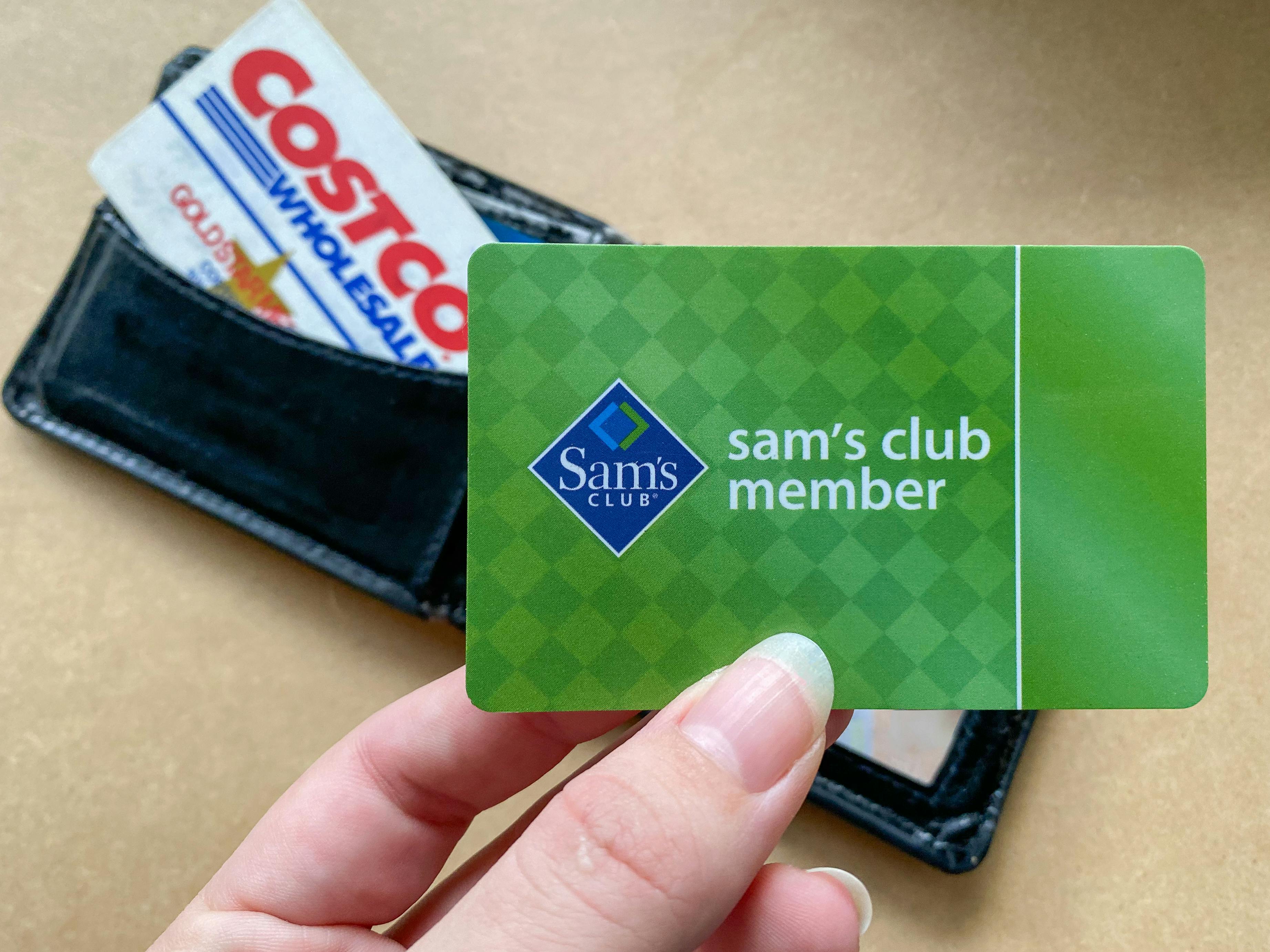 A person's hand holding a Sam's Club member card over a wallet with a Costco card in it.