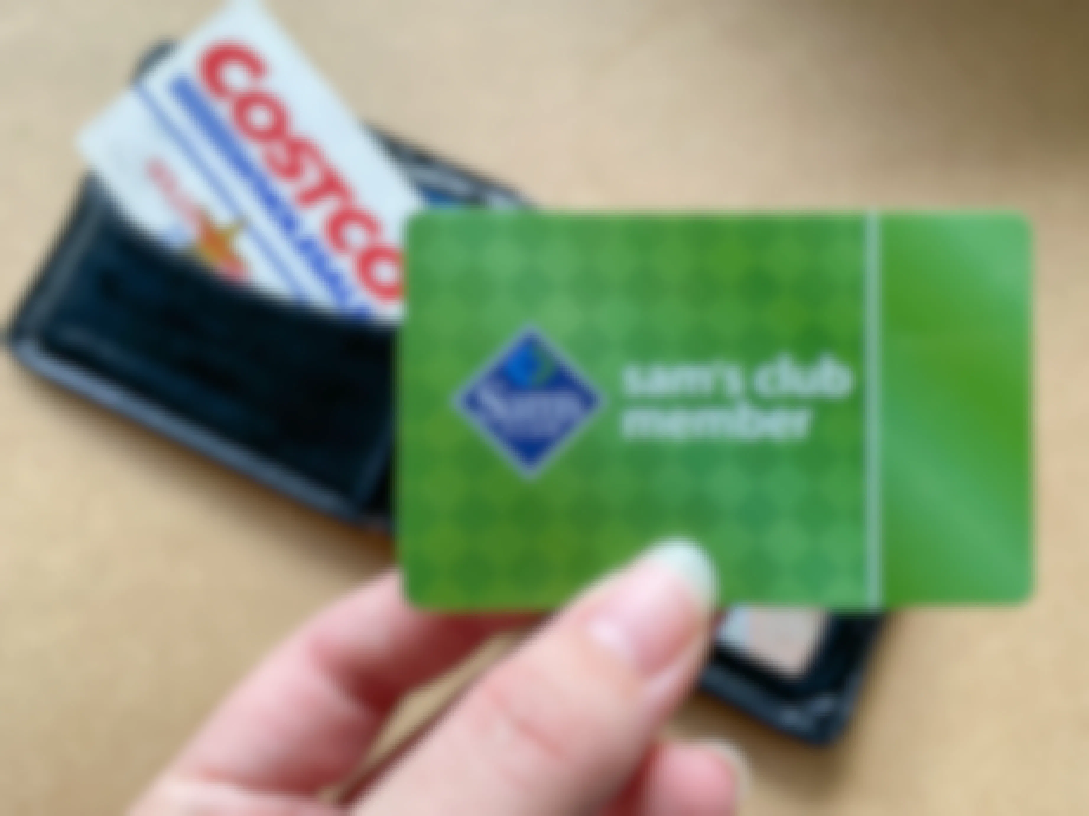 A person's hand holding a Sam's Club member card over a wallet with a Costco card in it.