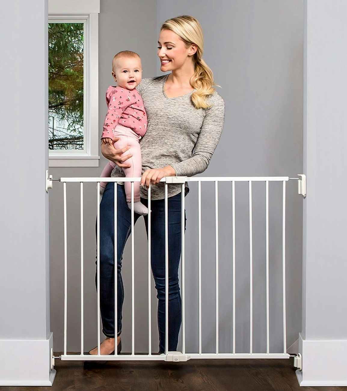 woman opening a top of the stairs baby gate holding a baby