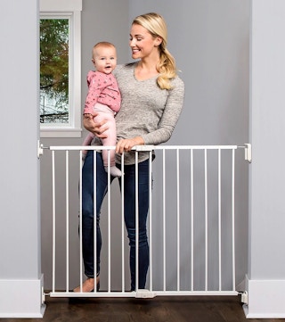 woman opening a top of the stairs baby gate holding a baby