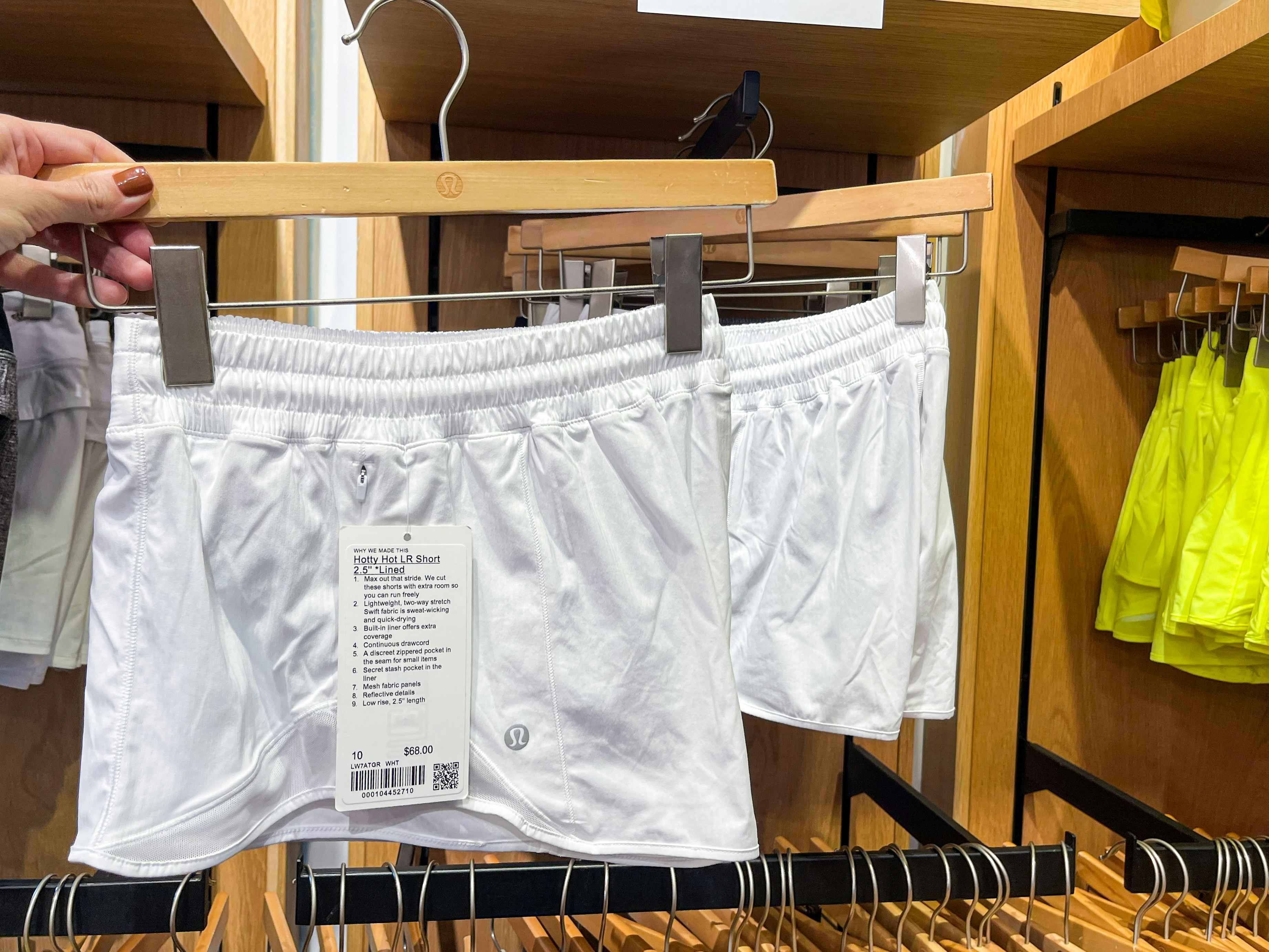 A pair of white work out shorts held out by hand in front of other shorts hanging on the store rack.
